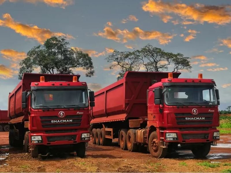 Deux camions bennes SHACMAN F3000 stationnés sur un site d’exploitation au coucher du soleil